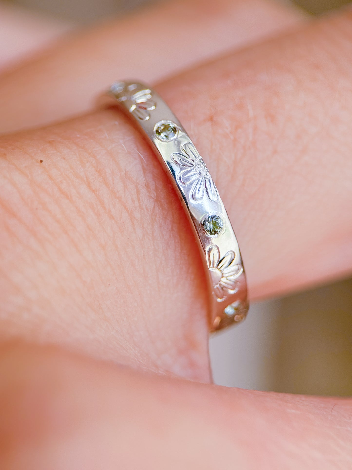 Anello artigianale Aurora Bariletti indossato, in argento 925, inciso a mano con margherite e zaffiri verdi dello Sri Lanka.