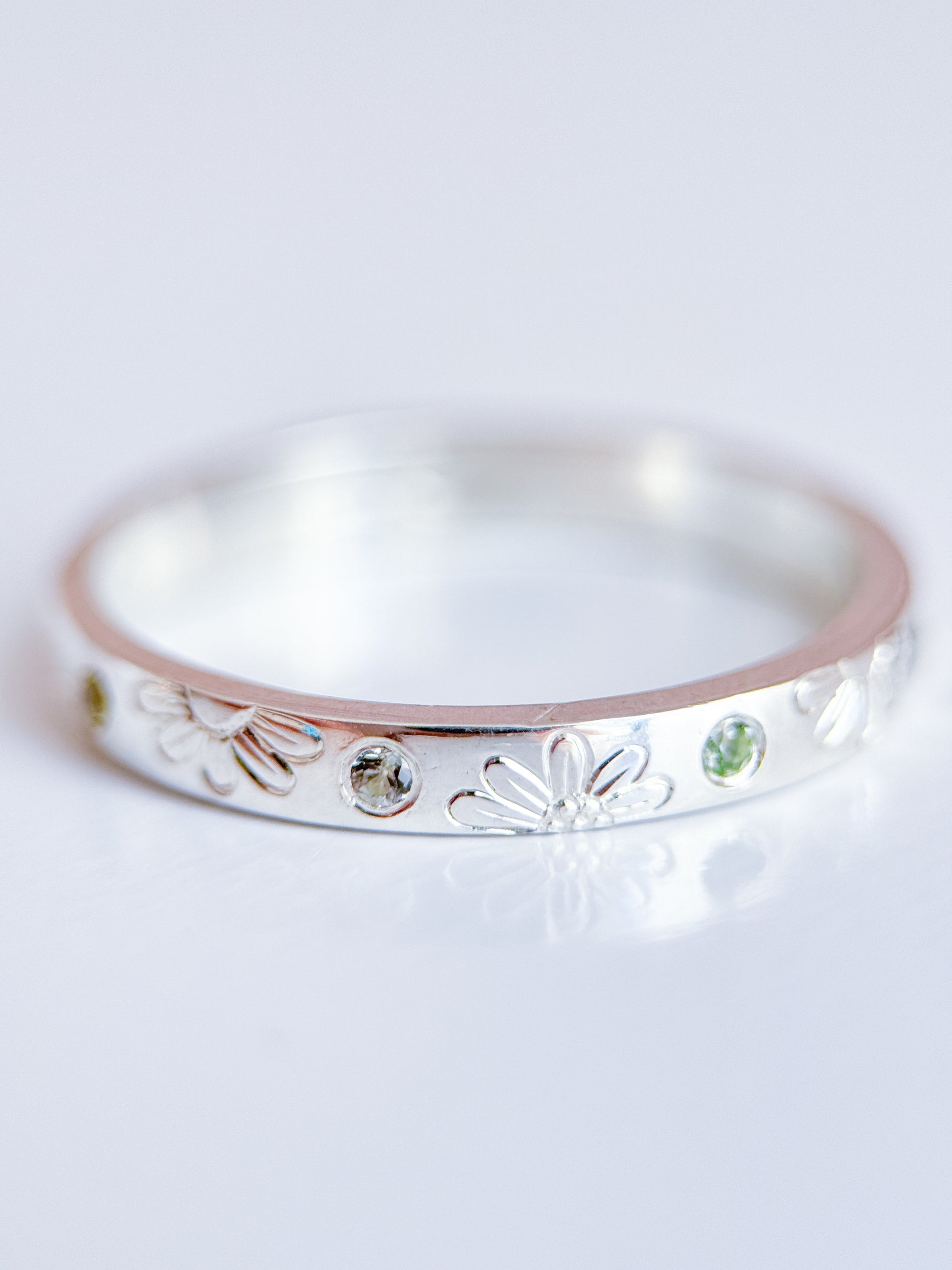 Anello artigianale Aurora Bariletti in argento 925, inciso a mano con margherite e zaffiri verdi dello Sri Lanka.