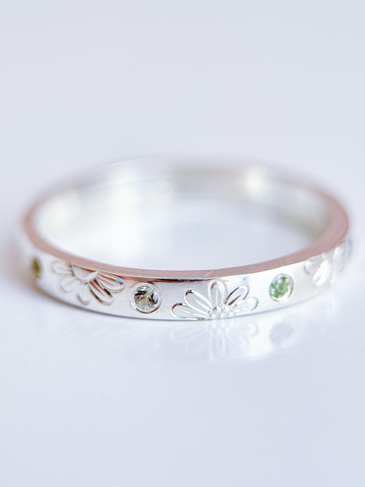 Anello artigianale Aurora Bariletti in argento 925, inciso a mano con margherite e zaffiri verdi dello Sri Lanka.