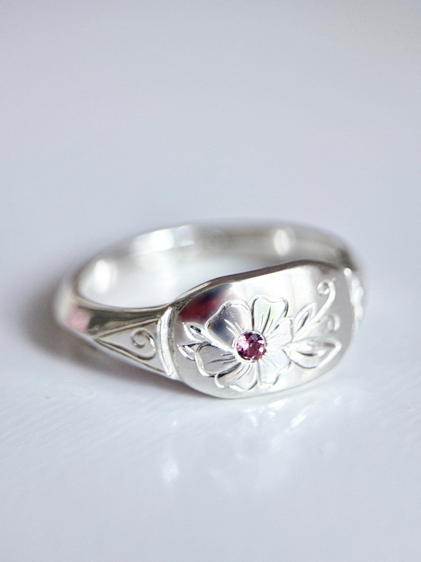 Anello artigianale esclusivo in argento 925, inciso a mano con un fiore centrale che accoglie una tormalina rosa. Creato con cura nel laboratorio di Aurora Bariletti.