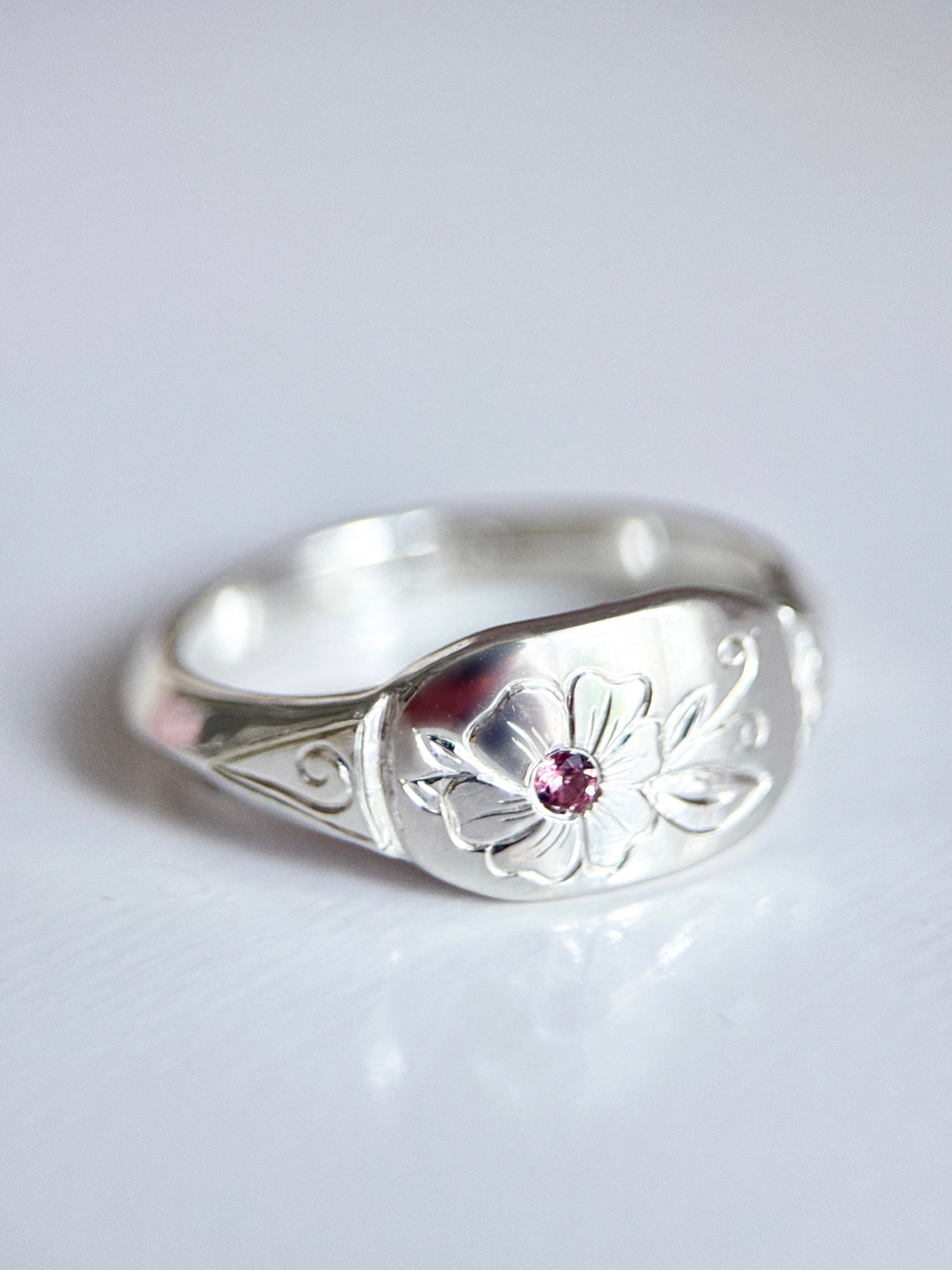 Anello artigianale esclusivo in argento 925, inciso a mano con un fiore centrale che accoglie una tormalina rosa. Creato con cura nel laboratorio di Aurora Bariletti.