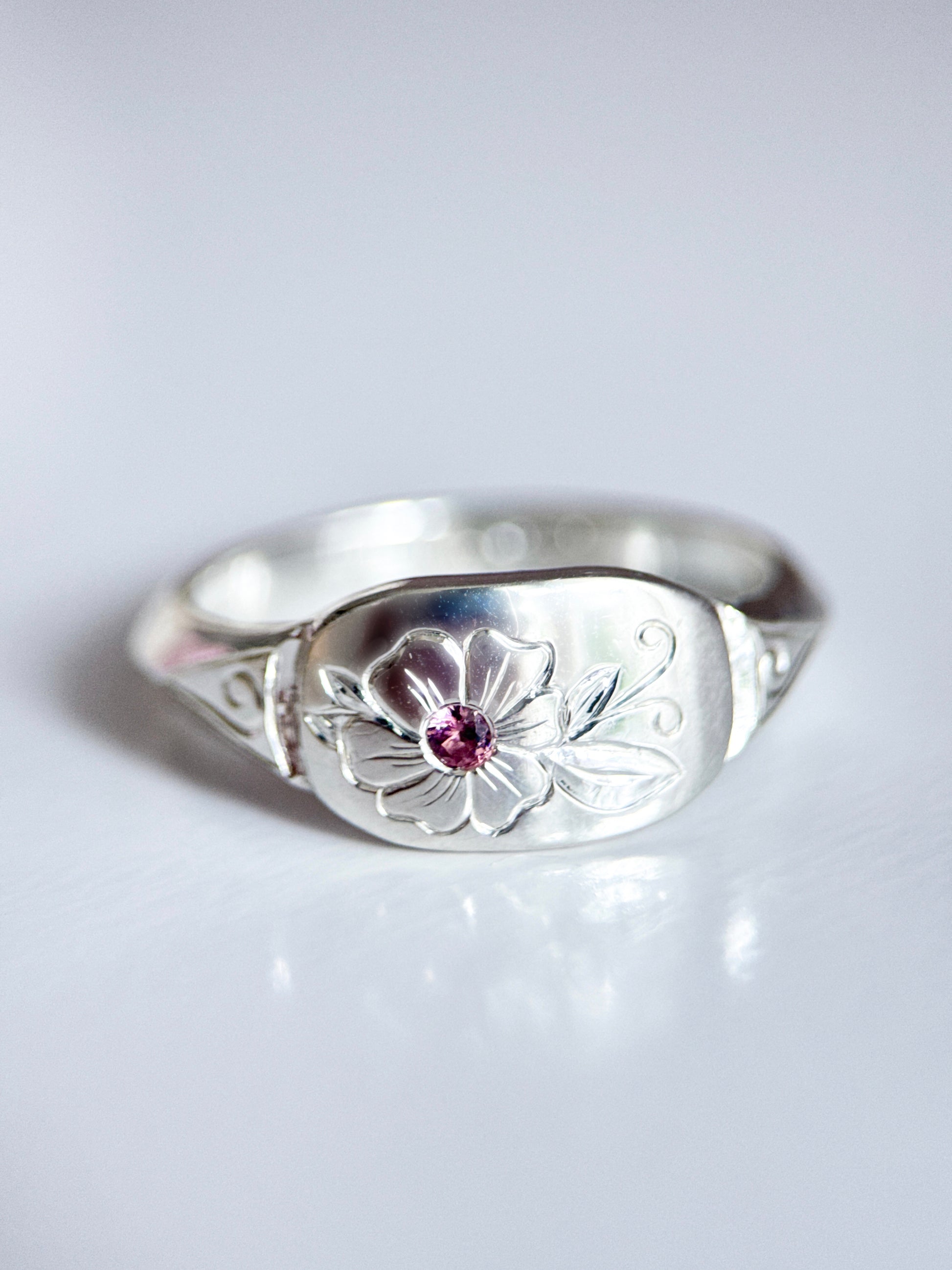 Anello artigianale esclusivo in argento 925, inciso a mano con un fiore centrale che accoglie una tormalina rosa. Creato con cura nel laboratorio di Aurora Bariletti.