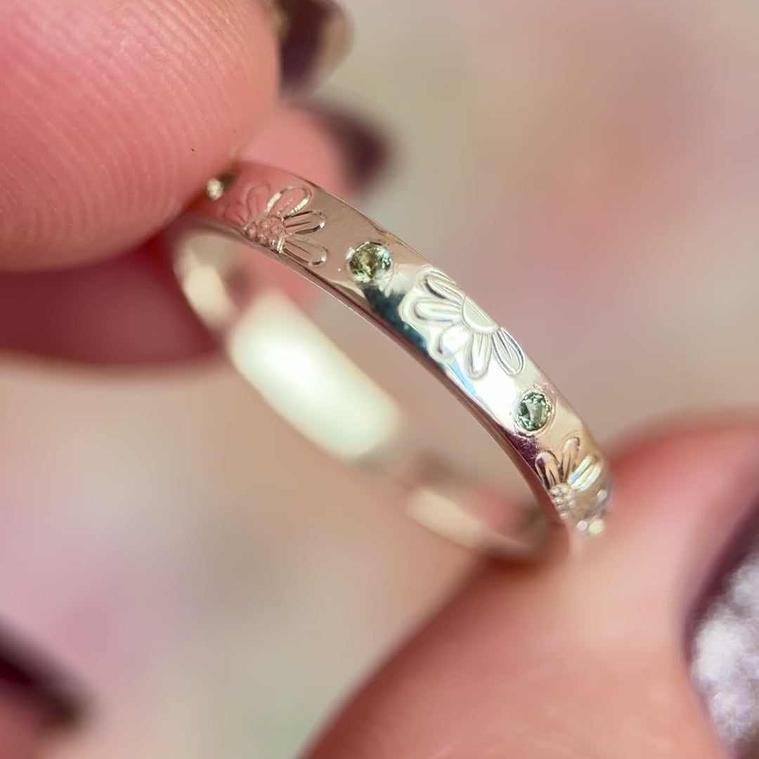 Anello artigianale Aurora Bariletti in argento 925, inciso a mano con margherite e zaffiri verdi.